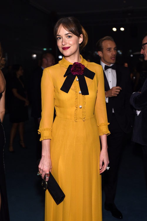 Dakota Johnson con vestido mostaza con lazada burdeos al cuello de la colección Crucero 2016